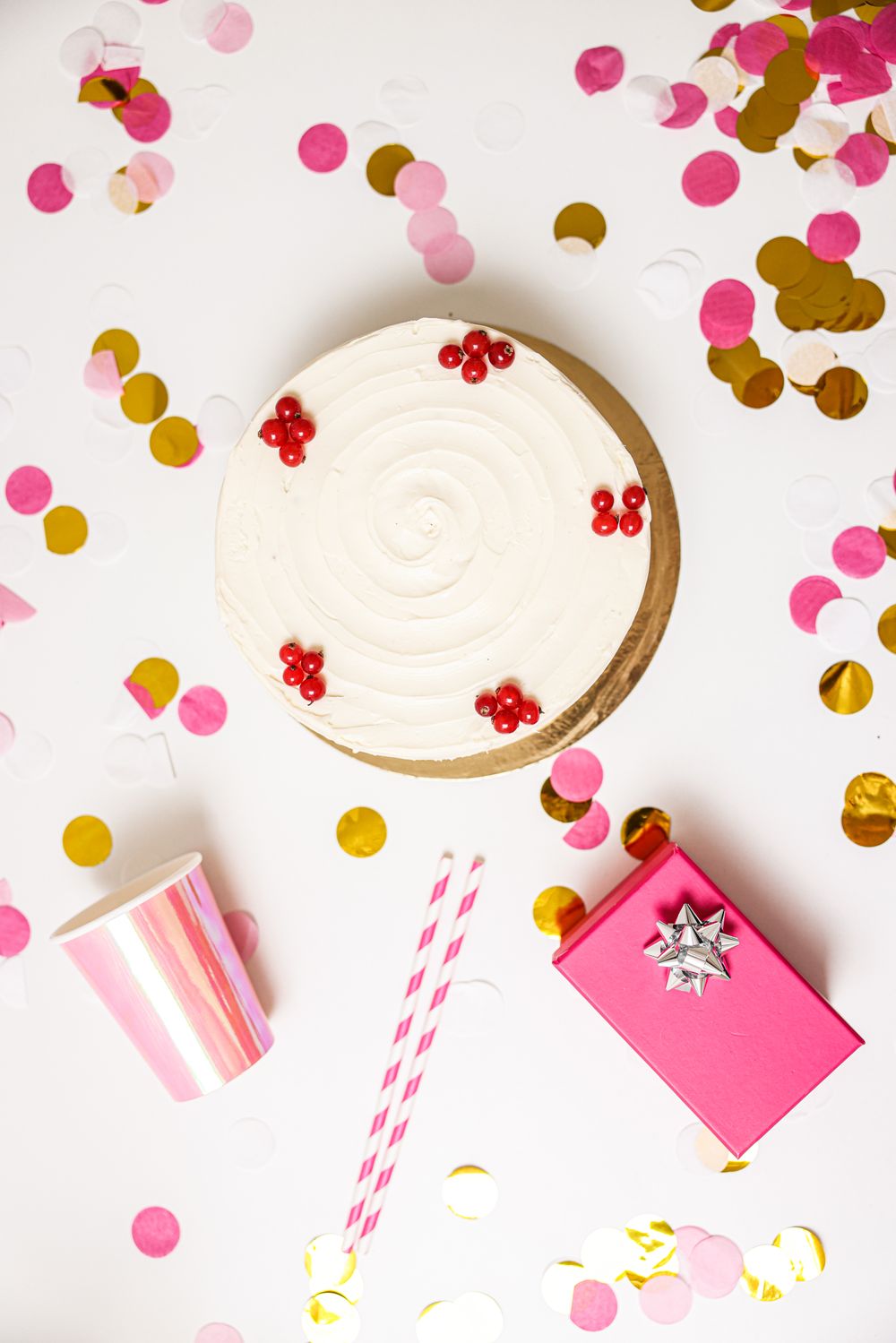 Top view of a birthday cake, confetti, straws and a small pink gift