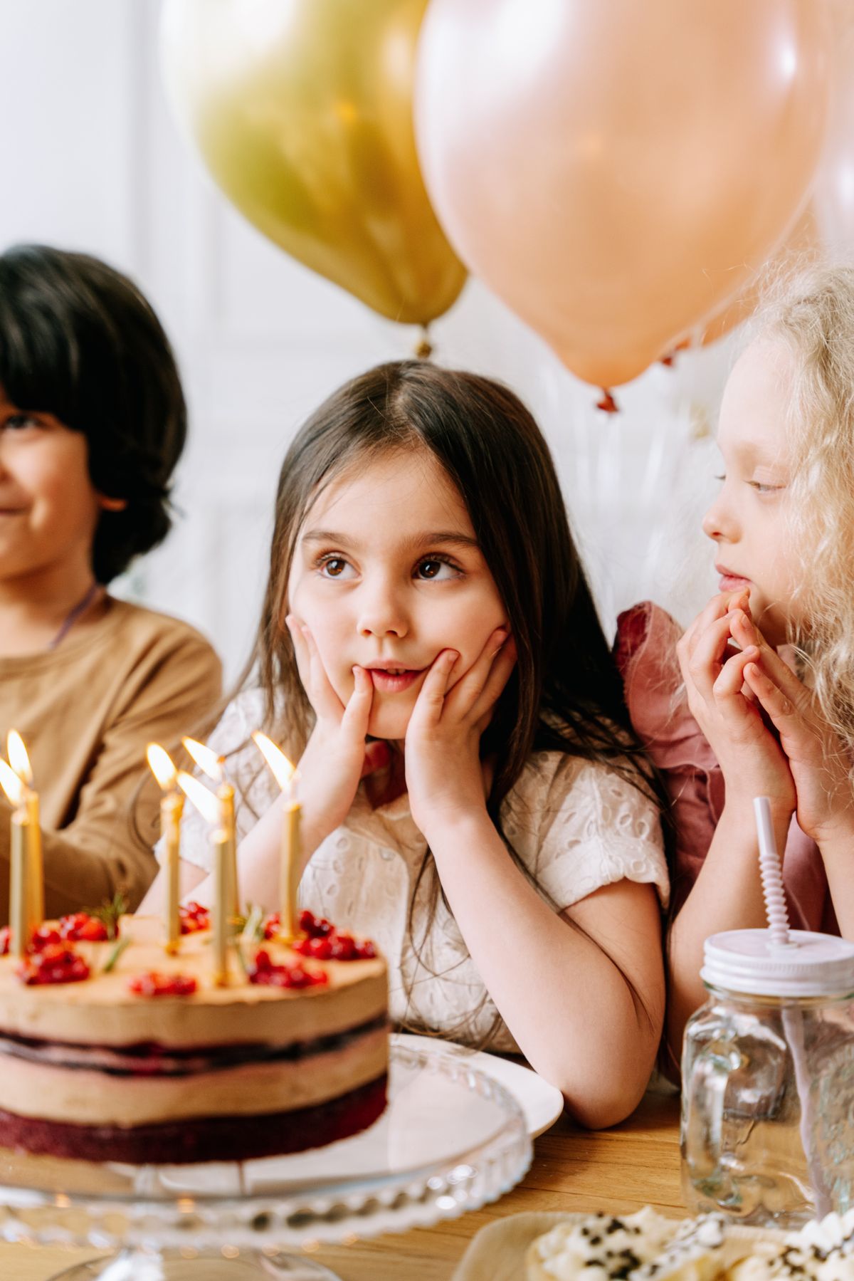 Children gathered around a birthday cake with candles and balloons